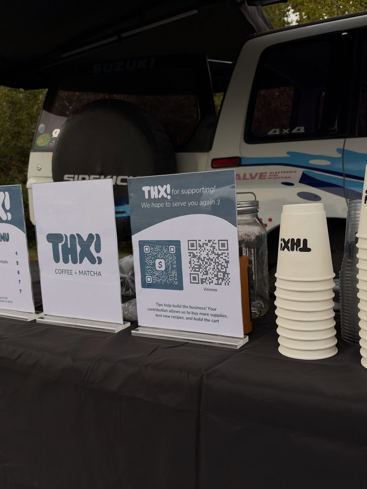 thx! acrylic sign stands and a tower of white thx! cups set up at a pop-up